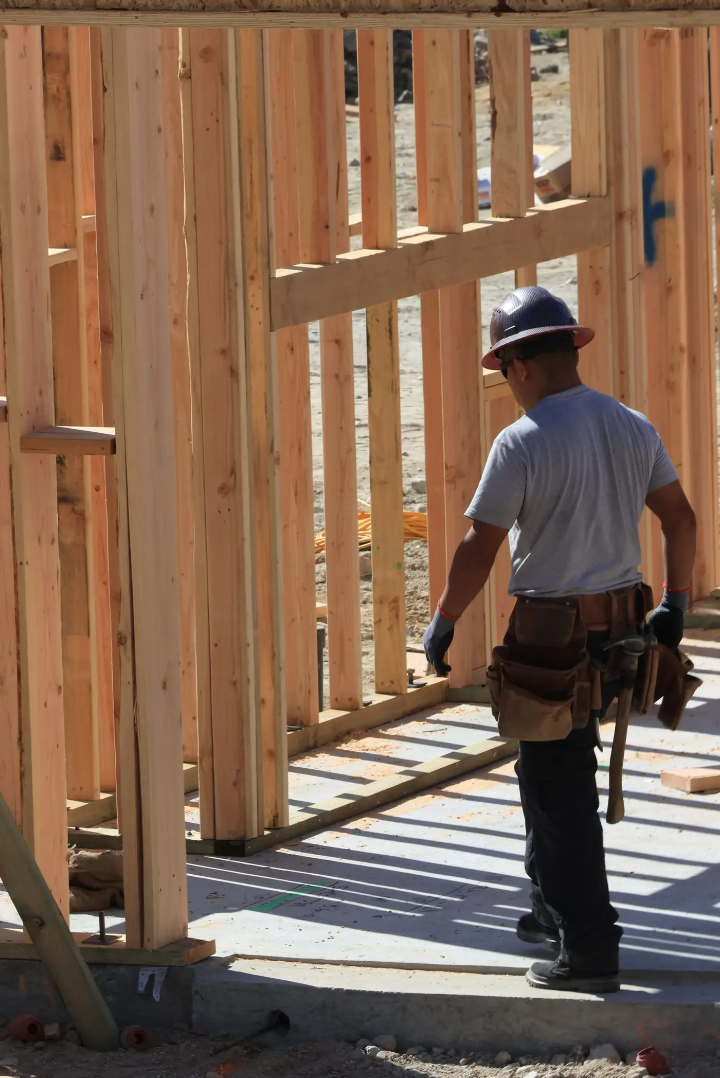 Carpenter in a hard hat and tool belt framing a timber stud wall on site