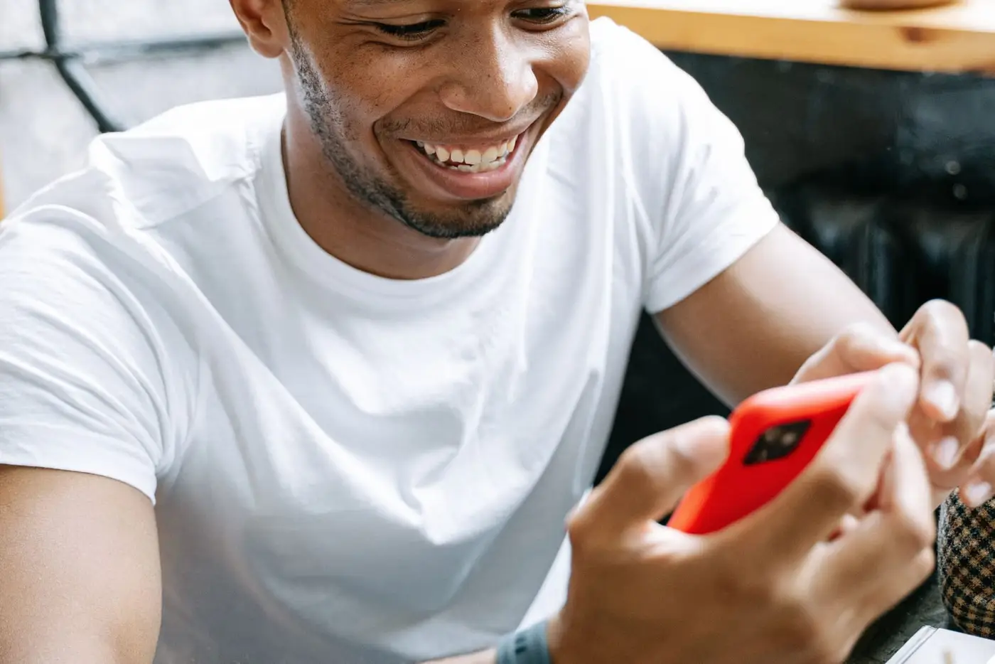 Homem rindo de algo no celular em uma mesa de café