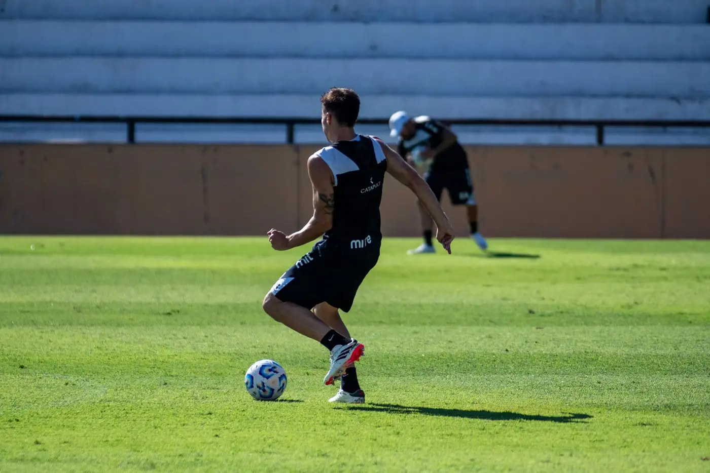 Jogador de futebol correndo para a bola em um campo diante de arquibancadas vazias