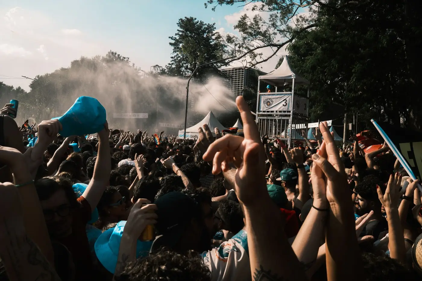 Crowd with hands in the air at an outdoor festival, cooled by water spray