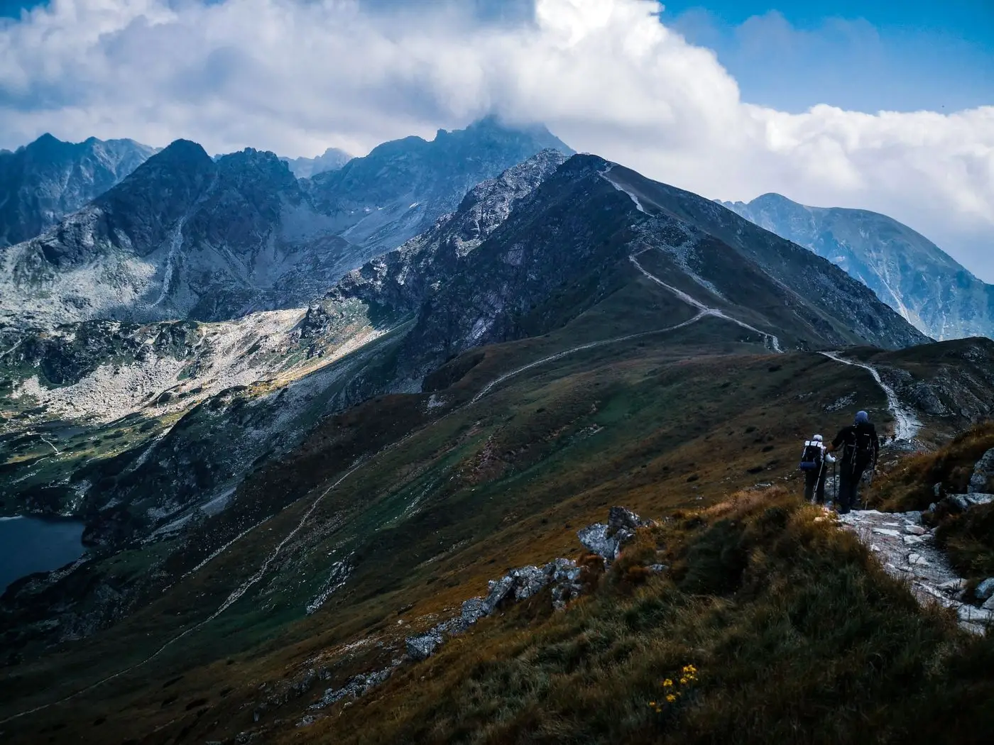Two hikers with backpacks following a ridge path high above a mountain valley