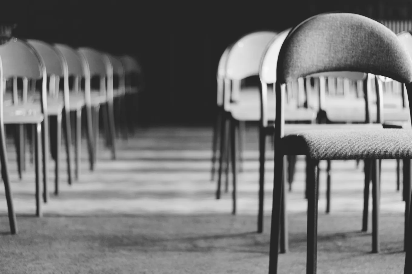 Rows of empty chairs in black and white, one chair in sharp focus