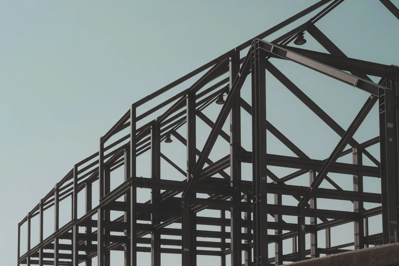 The steel frame of a building under construction against a pale sky